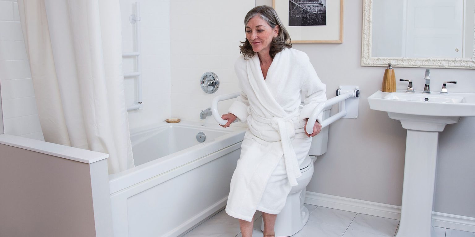 Woman standing up from a toilet while holding safety rails on both sides in a bright home bathroom